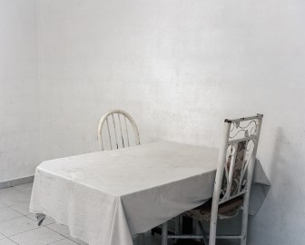 <em>ENDINGS_Table, white tablecloth and two chairs. Dominicks’s living room</em>, 2021-2024